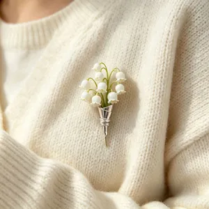Detail view of a French vintage lily of the valley brooch on a cream knit sweater.