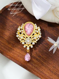 Close-up of a vintage-style gold brooch featuring a large pink teardrop crystal and rhinestones.