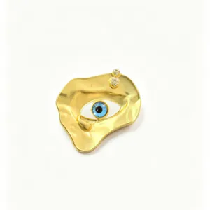 Detailed view of the irregular golden evil eye brooch with its blue crystal center.