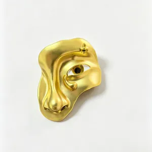 Detailed macro view of a surrealist golden face brooch with a realistic evil eye