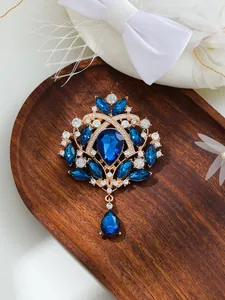 Detail view of an elegant vintage-style gold brooch featuring royal blue pear-cut crystals.
