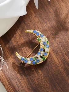 Detailed view of an exquisite gold crescent moon brooch with blue and clear rhinestones.