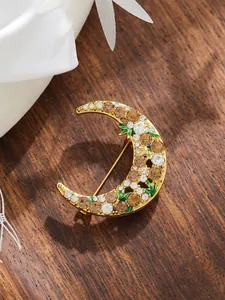 Macro detail of crescent moon brooch with champagne rhinestones and green enamel