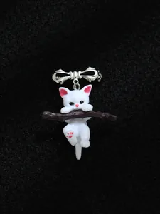 Detail van 3D witte hars kat speld aan een tak met een zilveren strikje.