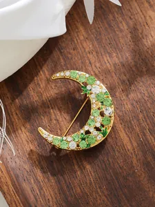 Detailed view of a golden crescent moon brooch with green and white rhinestones on wood