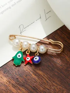 Detailed view of a golden safety pin brooch featuring white pearls and evil eye charms