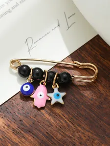 Detailed close-up of gold safety pin brooch with blue evil eye and pink Hamsa hand charms