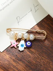 Detailed macro shot of a gold-tone safety pin brooch with pearls and evil eye charms