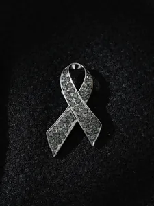 Κοντινό πλάνο καρφίτσας με γκρι στρας σε μαύρο ύφασμα, σε σχήμα κορδέλας μνήμης