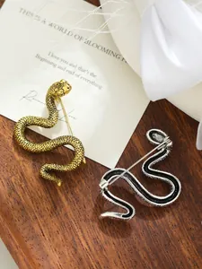 Vista detallada de broches con forma de serpiente en oro y plata sobre bandeja de madera.