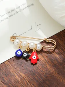 Detailed macro view of gold evil eye and Hamsa hand brooch pin decorated with white pearls
