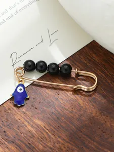 Detailed view of a gold Hamsa Hand brooch with black beads and blue evil eye charm