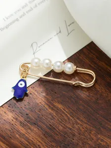 Detail showing gold-tone safety pin brooch with white pearls and blue evil eye hamsa charm.