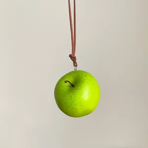 Vista detallada de un colgante de manzana verde realista en un cordón de cuero marrón