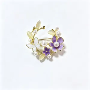 Gedetailleerde close-up van de elegante bloemenkrans broche met parels en paarse emaille bloemen.