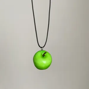 Primer plano detallado de un collar con colgante de manzana verde brillante en 3D.