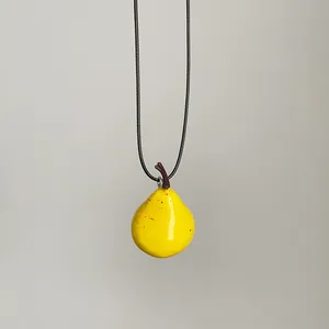 Detalle de un creativo collar con colgante de pera amarilla y cordón negro minimalista.