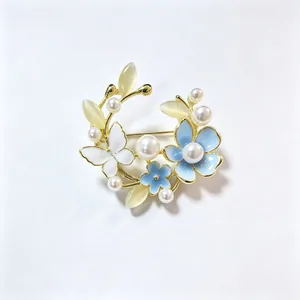 Detailopname van een ronde broche met blauwe bloemen, parels en kattenoogstenen in krans