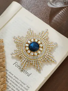 Nahaufnahme einer goldenen Sonnenblumen-Brosche mit blauem Kristall auf einem alten Buch