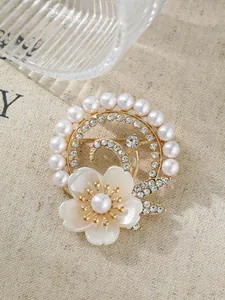 Detail einer eleganten goldfarbenen Brosche mit Perlen, Strass und weißem Blumenmuster.