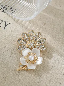 Detailaufnahme einer eleganten Blumenbrosche mit Perle und funkelnden Kristallen in Gold.
