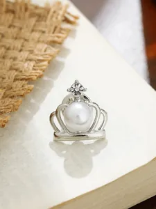 Detaillierte Makroansicht einer silbernen Kronenbrosche mit weißer Perle und Strassstein.