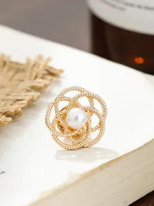 Nahaufnahme einer goldfarbenen Kamelien-Brosche mit einer eleganten zentralen Perle
