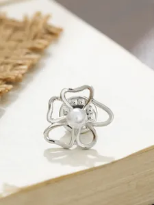 Makroansicht einer silbernen Blumenbrosche mit weißer Perle auf einer Buchseite.