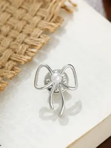 Makro-Detail einer eleganten silbernen Schleifennadel mit Perle auf einer Buchseite