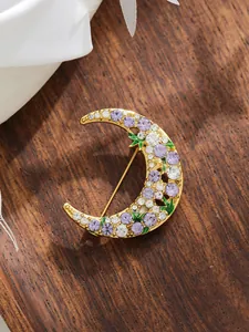 Detailed view of a crescent moon brooch with purple and white crystals on a wooden surface.