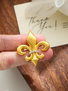 Detailed view of a vintage gold fleur-de-lis suit brooch with sparkling rhinestones