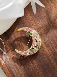 Close-up detail of a crescent moon brooch with pink rhinestones and gold finish