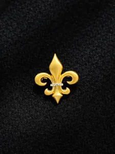 Detail view of golden fleur-de-lis brooch with shiny crystals on black fabric