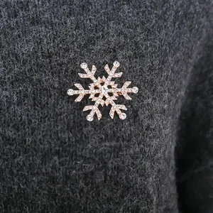 Detailansicht einer funkelnden Schneeflocken-Brosche mit Strass auf grauem Pullover
