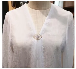 Detailaufnahme einer geometrischen goldenen Brosche an einer weißen Bluse mit V-Ausschnitt