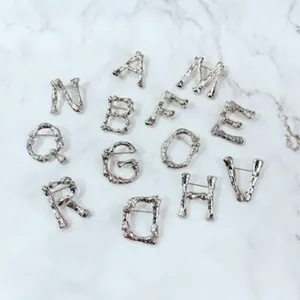 Vielfältige Kollektion silberner strukturierter Alphabet-Broschen auf Marmorhintergrund
