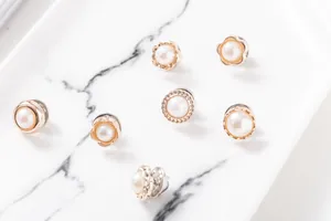 Primer plano de varios broches decorativos de perlas y tono dorado en bandeja de mármol