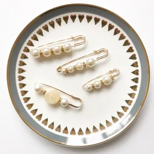 Elegante goldfarbene Sicherheitsnadel-Broschen mit Perlen und Strasssteinen auf Teller