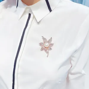 Detailansicht einer eleganten goldenen Blumenbrosche mit Perle und Kristallen auf Hemd