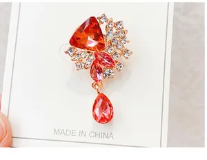 Detailed view of a red crystal brooch featuring a dangling teardrop gem and stones