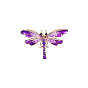 Vintage dragonfly brooch with purple enamel wings and central gemstone on gold frame