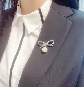 Dettaglio di una spilla a fiocco argento con perla bianca sul risvolto di un blazer nero.