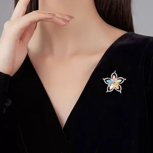 Detailansicht einer bunten Blumenbrosche mit Strass auf einem schwarzen V-Ausschnitt-Kleid.