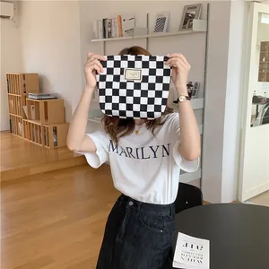 Close-up of black and white checkerboard canvas pouch held in a minimalist interior
