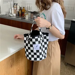 Detail view of a black and white checkered canvas tote bag held by a person.