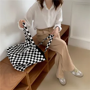 Close-up of a large black and white checkerboard canvas tote bag held by a model