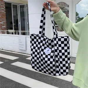 Detail view of a large black and white checkered canvas tote bag held in an urban street setting