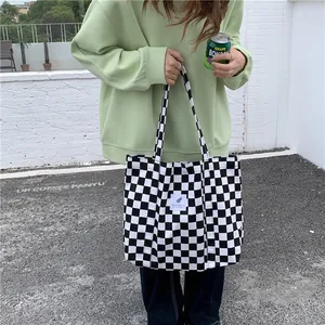 Detail of a chic black and white checkerboard canvas tote bag held by a model