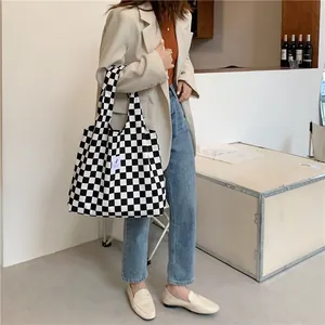 Detailed view of large black and white checkerboard canvas tote bag held by model