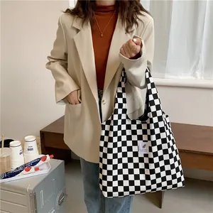 Chic black and white checkerboard canvas tote bag held by a model in a beige blazer.